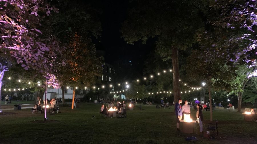 Students sit around fire pits on the campus green.